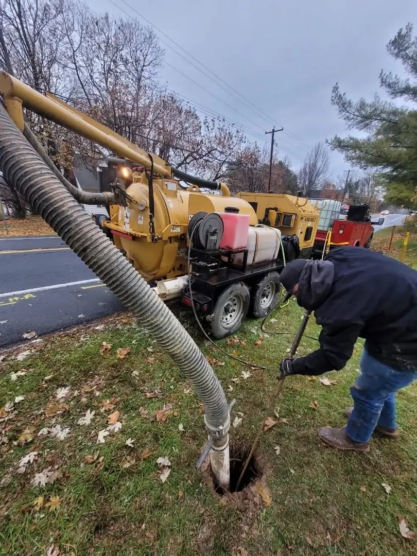 Crew member guiding a hydro excavation hose at a roadside utility dig