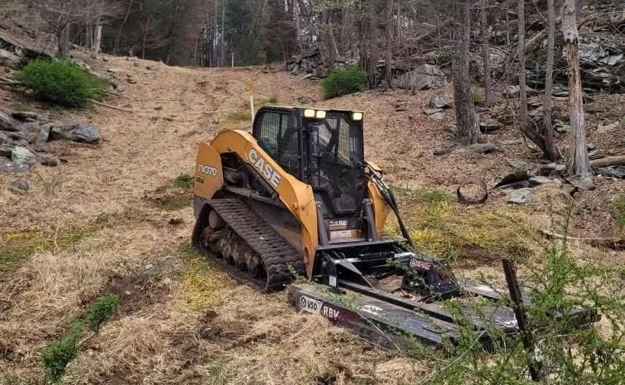 Site work crew clearing brush on a wooded hillside with a tracked mulcher